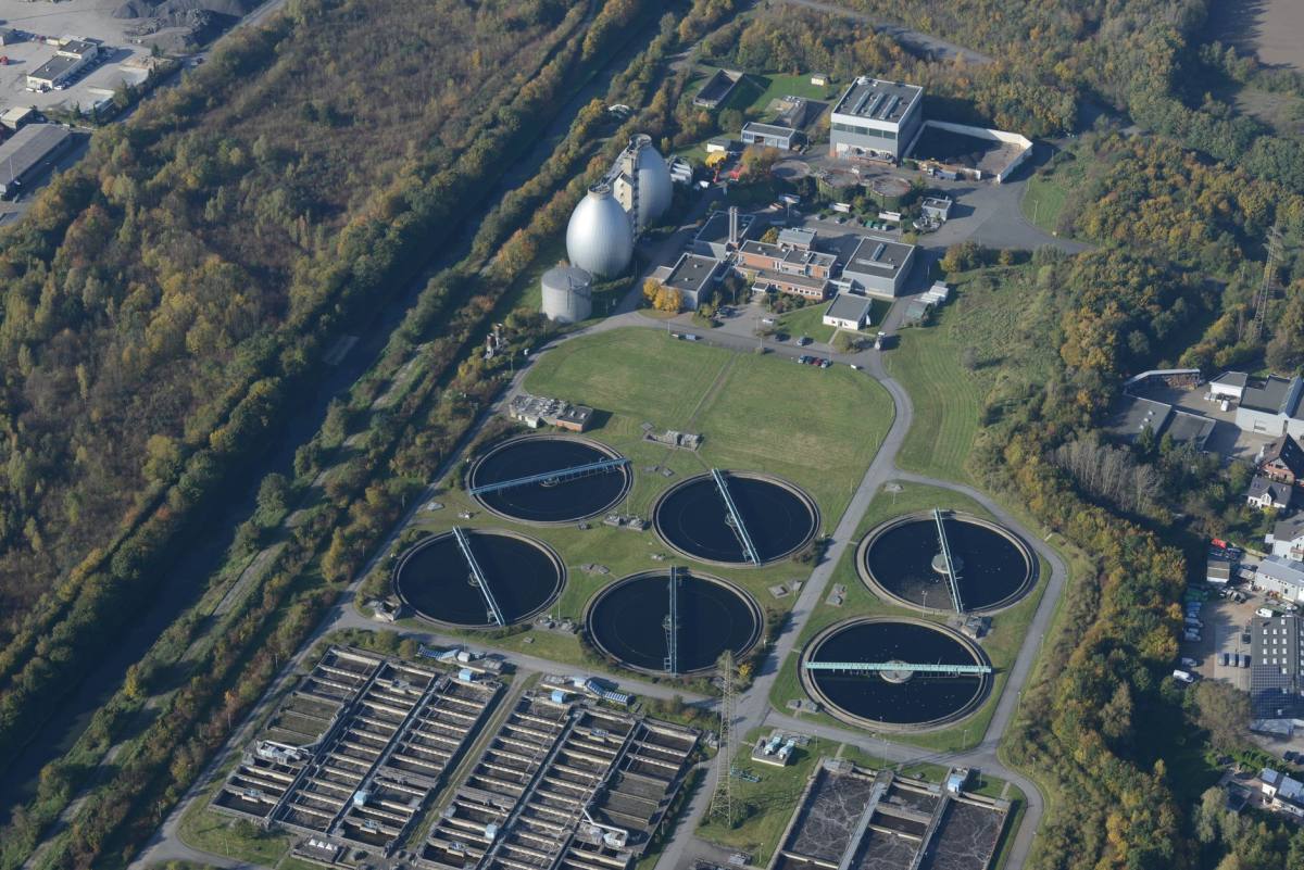 Aerial view of circular clarifier tanks and process buildings at a wastewater treatment plant surrounded by autumn trees
