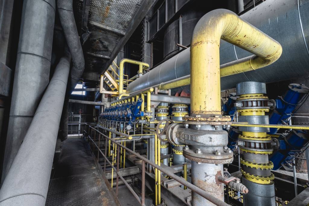 Yellow and grey steel pipework with valves and flanged joints inside an industrial process hall