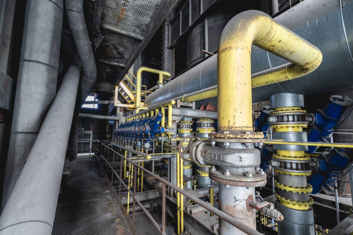 Yellow and grey steel pipework with valves and flanged joints inside an industrial process hall