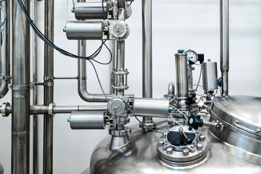 Close-up of a stainless steel process vessel with pneumatic valve actuators, pipework and a pressure gauge