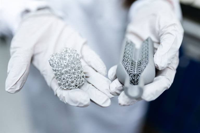 SENZAIT Advanced manufacturing — a three-dimensionally printed metal lattice structure held in a gloved hand in a laboratory.