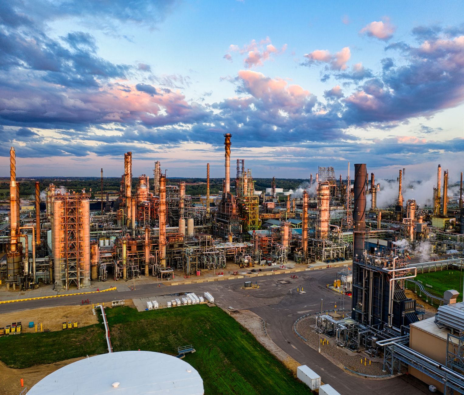 SENZAIT Industries served — a refinery's columns, flare stacks and pipe racks under an evening sky, seen from the air.