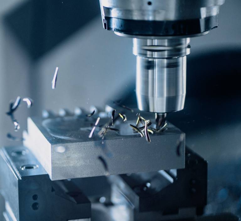 SENZAIT Precision CNC machining — close-up of a metal cutting tool mounted in a CNC machine, with swarf thrown from the cut.