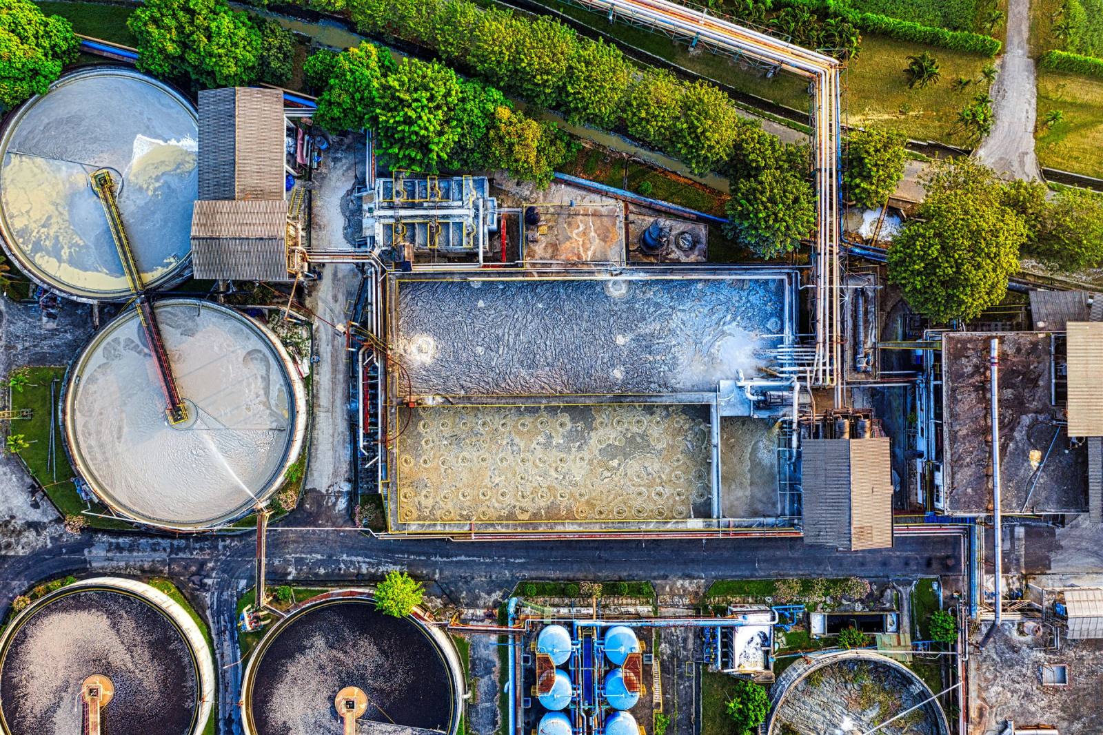 SENZAIT Waste water treatment plant — top-down view of circular clarifiers, an aeration basin, and a diffused-aeration basin with the diffuser grid visible in the bubble pattern.