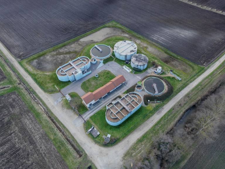 SENZAIT Water and wastewater — aerial view of a compact wastewater treatment works: circular clarifiers, a digester and the control building beside open fields.